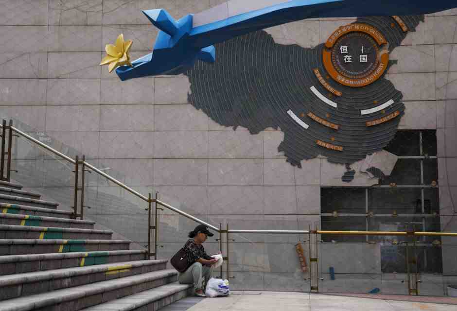 Una donna sistema la spesa vicino a una mappa che mostra i progetti di sviluppo di Evergrande, Pechino, 18 settembre 2023 (AP Photo/Andy Wong)&nbsp;<br />