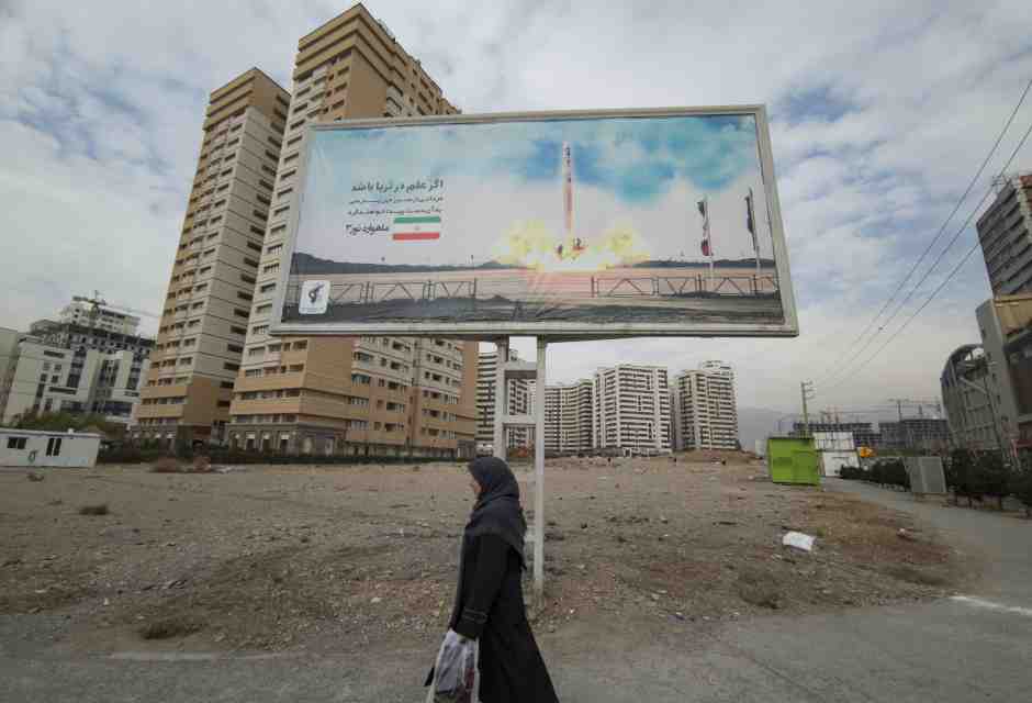 Una donna cammina sotto un cartellone della compagnia satellitare iraniana Qased in una zona residenziale di Teheran (Morteza Nikoubazl/NurPhoto) <br />
