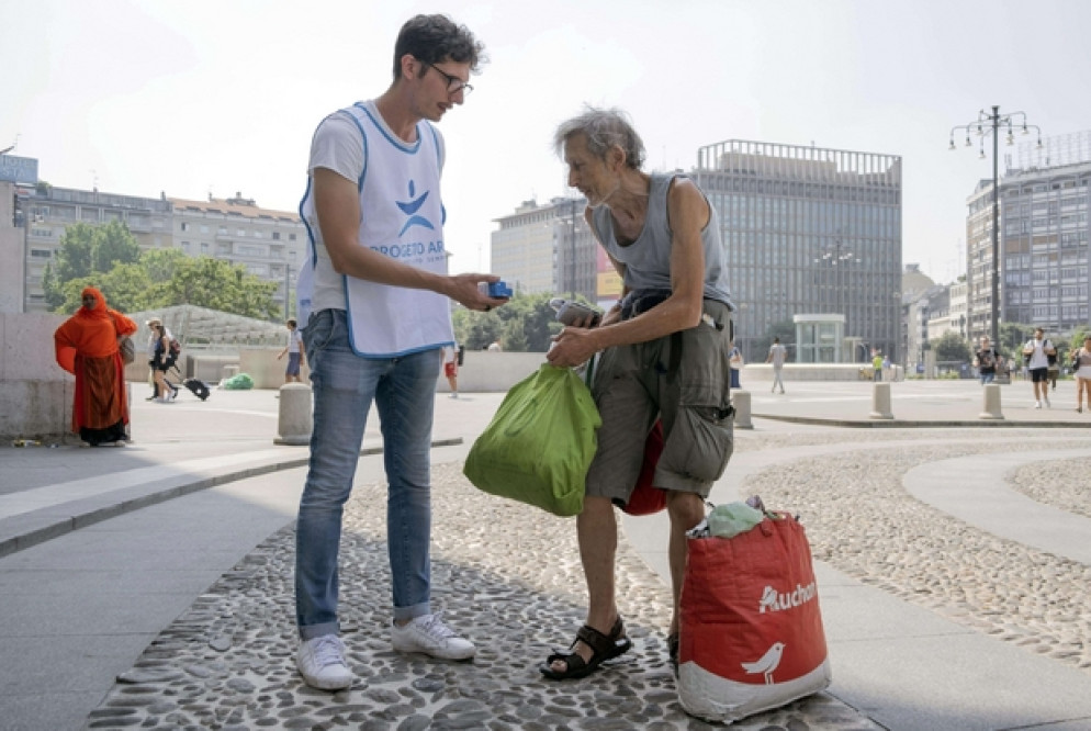 Un giovane volontario del Progetto Arca consegna un succo di frutta fresco a un senza fissa dimora nel centro di Milano, ieri ancora tra le città da bollino rosso per le temperature da record. L’afa, e la mancanza di ricoveri attrezzati d’estate, mettono a rischio i clochard