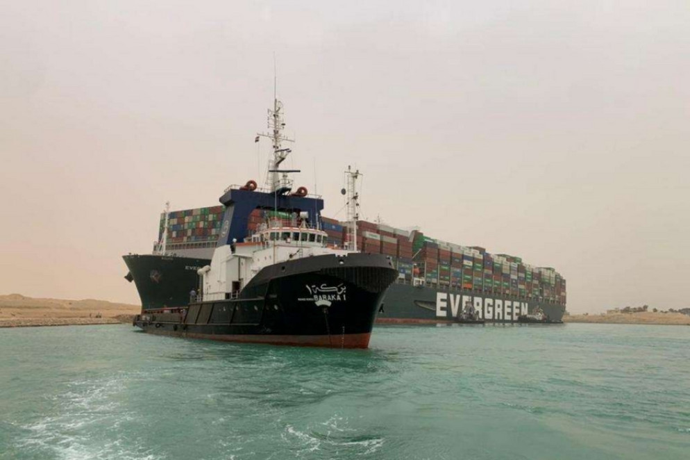 Un'immagine del cargo incagliatosi nel Canale di Suez, sullo sfondo, e in primo piano un'imbarcazione di soccorso - Reuters