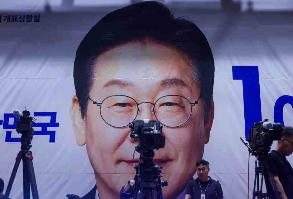 I cameraman sistemano le loro attrezzature davanti a uno striscione con il volto del candidato presidenziale Lee Jae-myung (Daniel Ceng/Getty Images)<br />